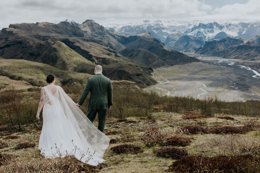 bride and groom walking in iceland with expansive mountainous view in background