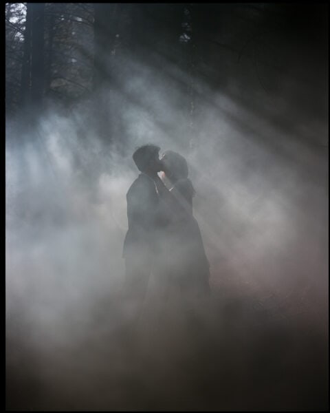 groom and bride is kissing in the foggy moody pine forest