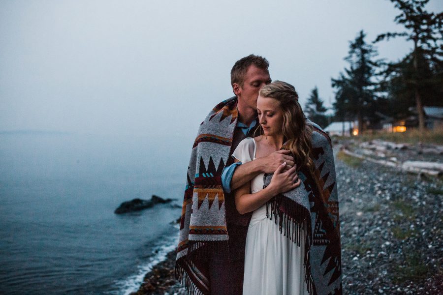 A bride and groom snuggle under a blanket at dusk on orcas island photographed by Amy Galbraith