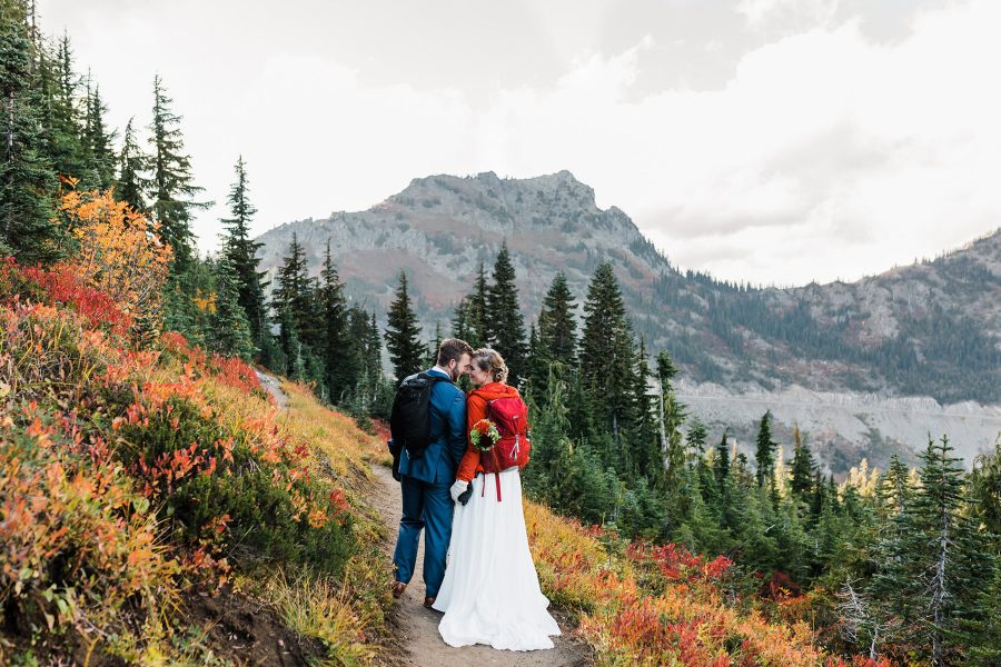 a bride and groom walk down a trail near Mt Rainier backdropped by autumn colors after their elopement on the Pacific Crest Trail