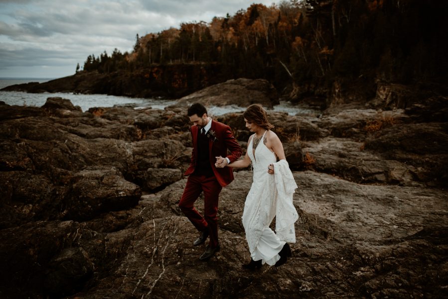 Wedding couple walking across the black rocks on Presque Isle in Marquette