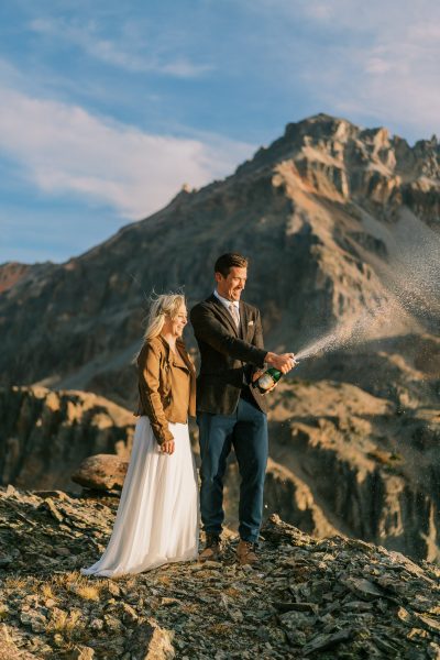 Couple pops a bottle of champagne on a Colorado mountain top.