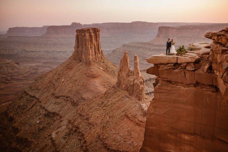 A bride and grooms stand cliffside in Moab, Utah
