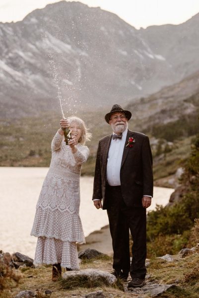 An older couples celebrates their Colorado elopement by popping a bottle of champagne in front of a lake.