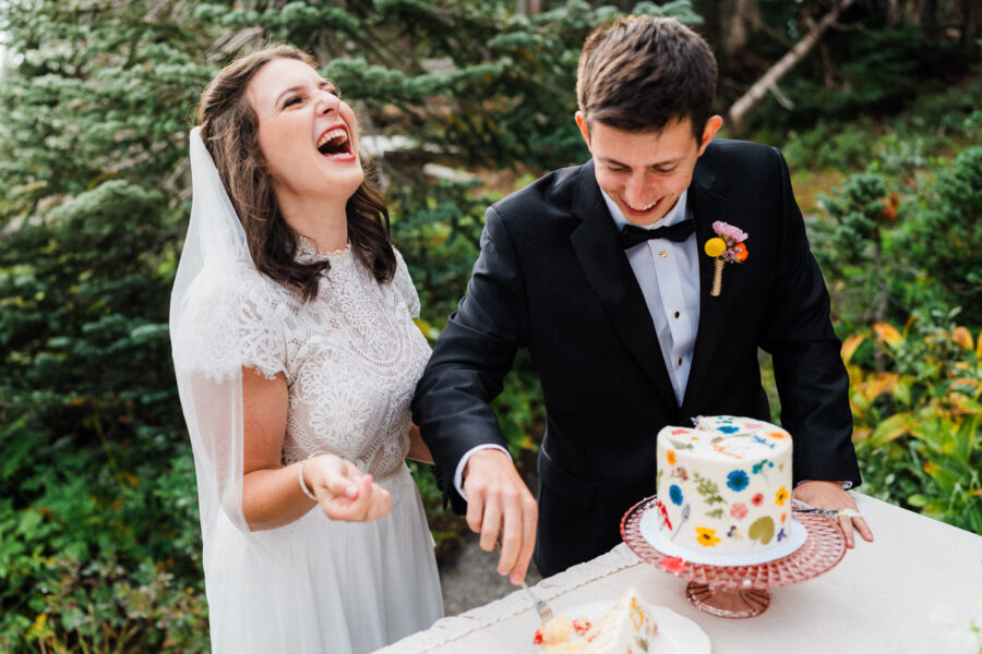married couple laughing while cutting wedding cake