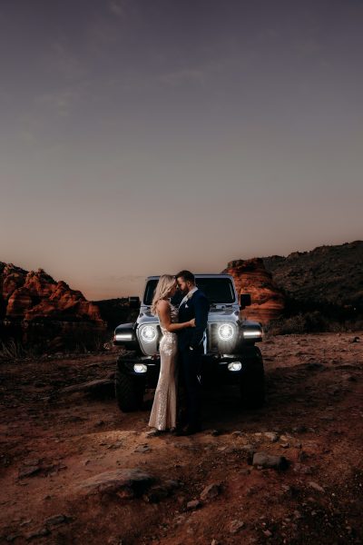 Bride and Groom holding each other in front of a jeep wrangler surrounded by the desert after eloping at Merry Go Round Rock in Sedona AZ