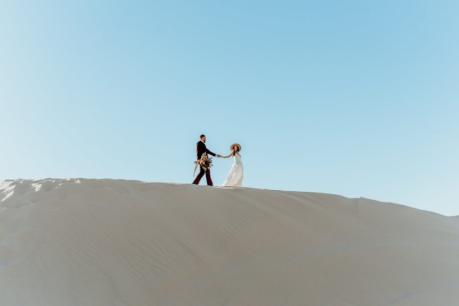 bride leading groom atop a sand dune outside Yuma Arizona
