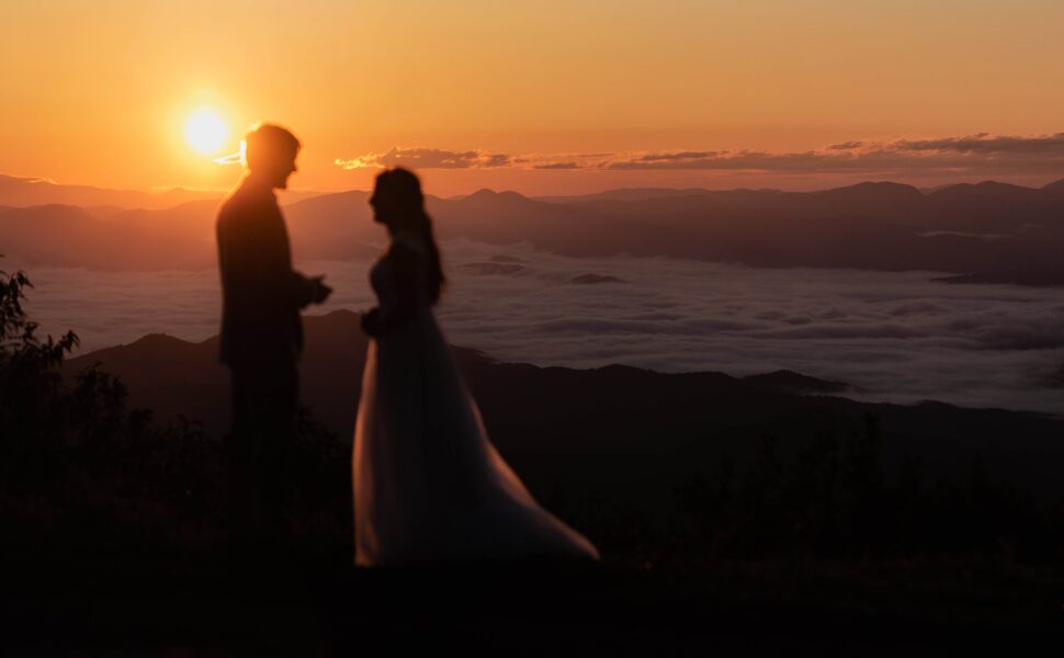 A silhouetted newlywed couple enjoying the sunrise mountain view overlooking a cloud inversion