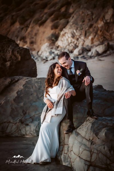 A bride and groom sitting on a very big rock on the beach during blue hour at their Big Sur Adventure Elopement