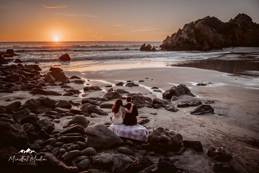 A bride and groom sitting on a rock overlooking Pfeiffer Beach in Big Sur for their Adventure Elopement in Big Sur, CA
