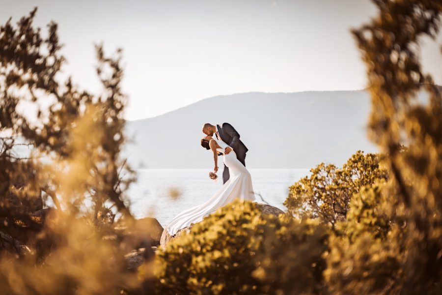 A wedding couple doing the dip standing on a giant boulder in front of Lake Tahoe for their elopement