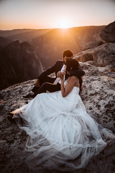 A wedding couple embracing and hugging on a rock with the sunset directly behind them for their Yosemite Adventure Elopement