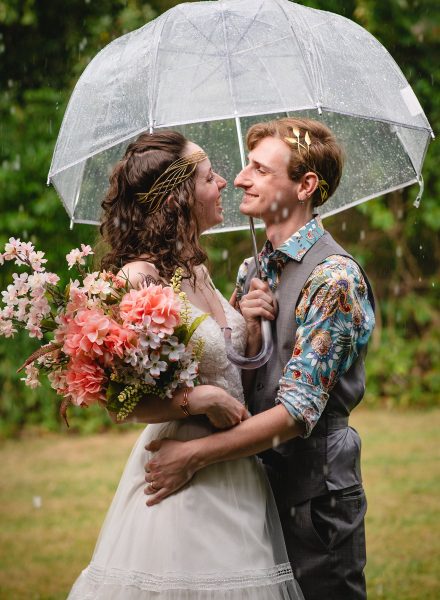 wedding couple embracing under umbrella in the rain