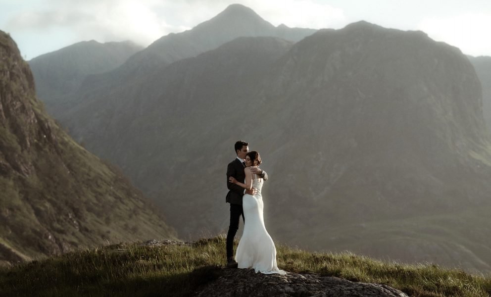 bride and groom standing in the afternoon sun between the mountains of Glencoe during their elopement in Scotland