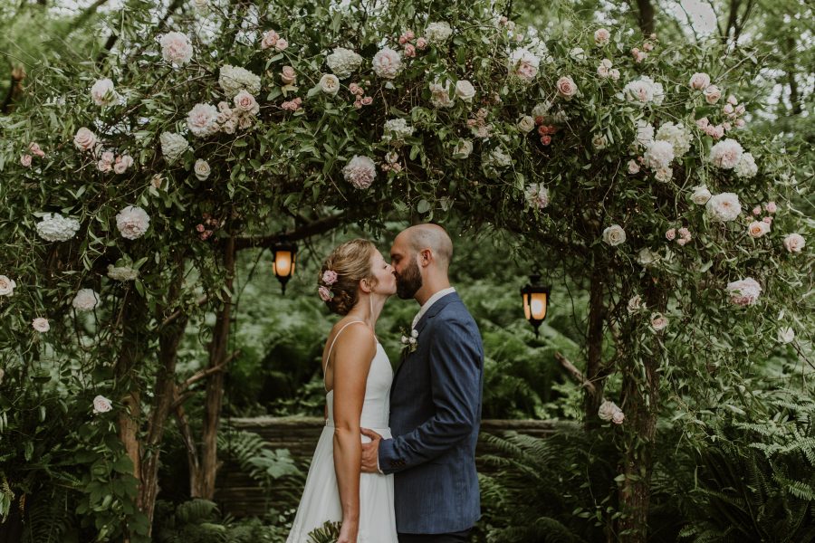 couple marrying and kissing under flower arch