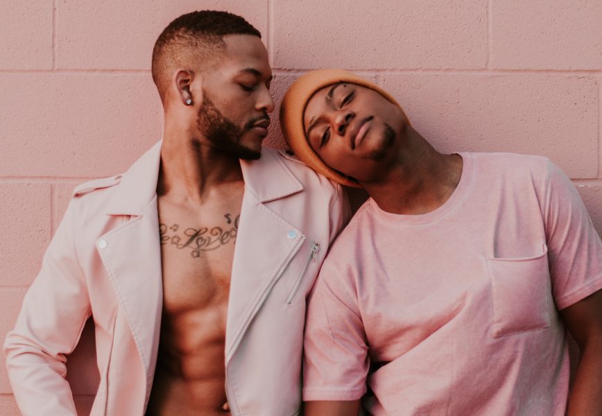 gay couple in pink sitting at pink wall leaning on one another