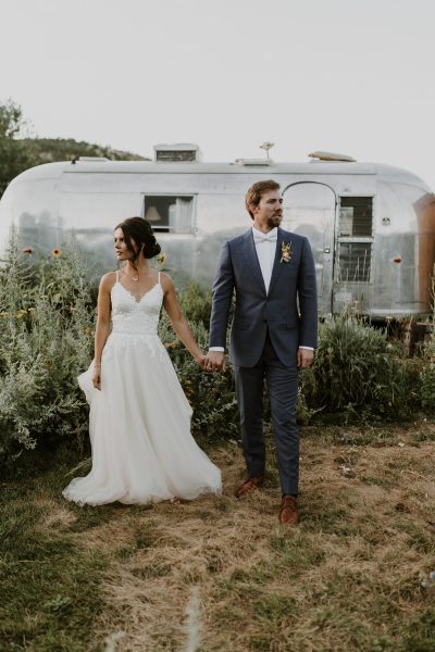 couple in wedding attire holding hands in front of an airstream