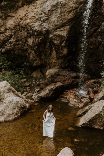 bride standing in water next to waterfall