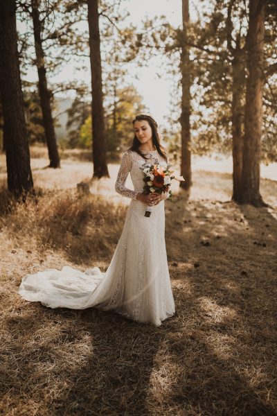 bride holding bouquet and standing among pine trees