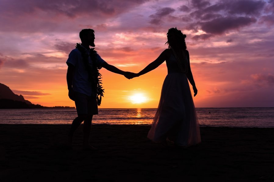 Bride and groom strolling under a gorgeous sunset on Hanalei Bay in Kauai, Hawaii
