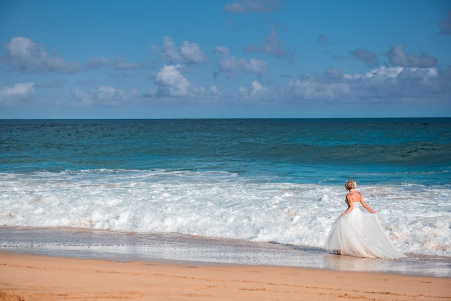 Bride plays in the waves in her wedding dress on a secluded beach in Kauai, Hawaii