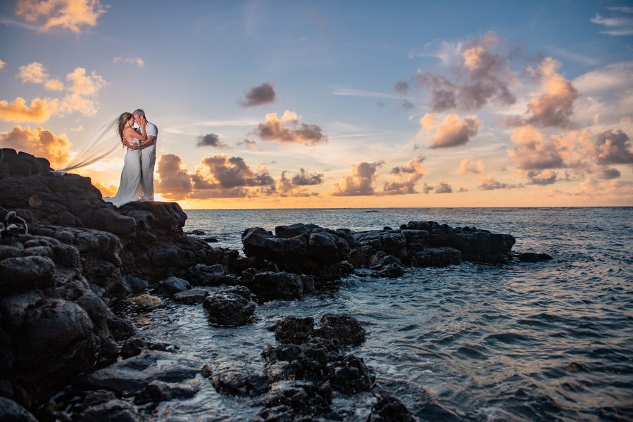 Bride and groom snuggling on a black lava cliff on a beach at sunset in Kauai, Hawaii