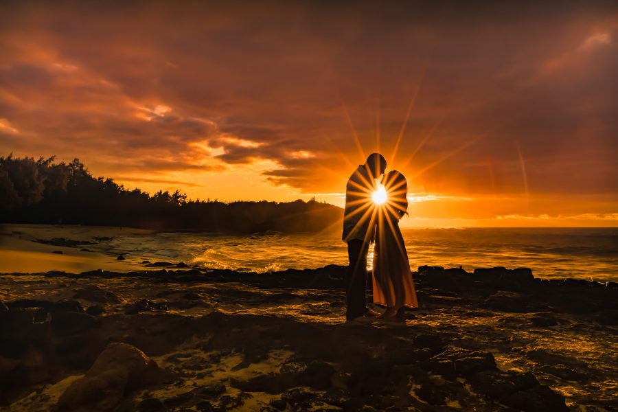 Bride and groom silhouetted in a sunstar at sunrise on a beach in Kauai, Hawaii