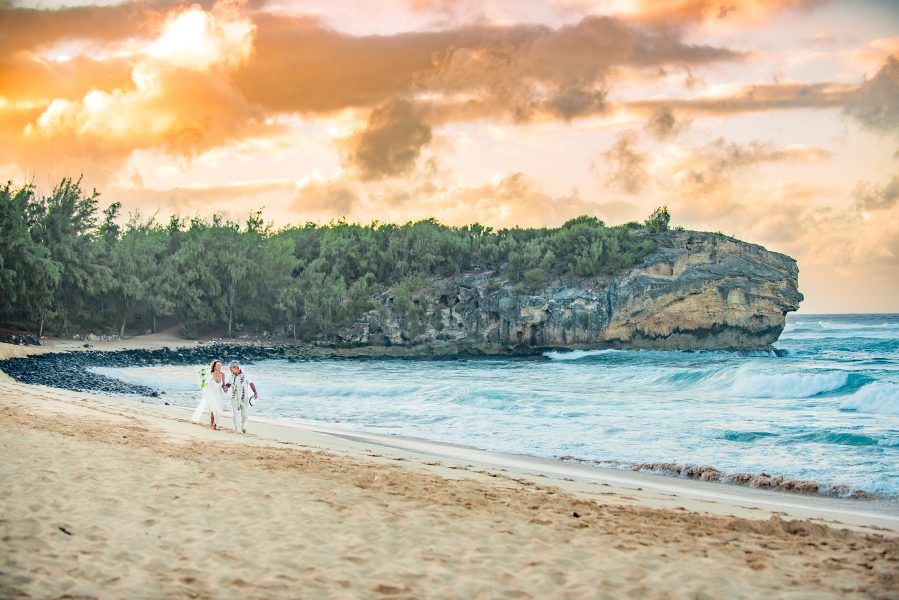 Bride and groom walking on an empty beach at sunrise in Kauai, Hawaii