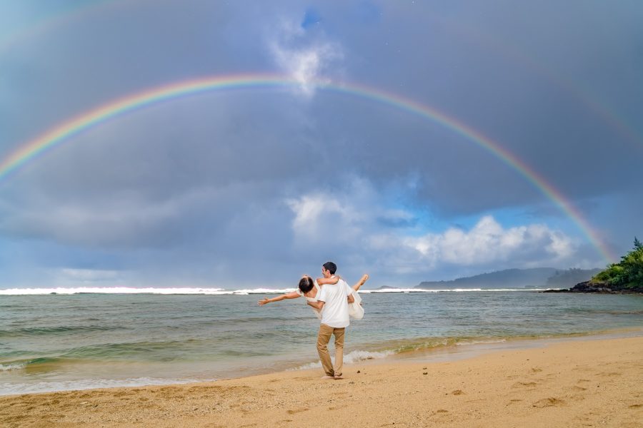 Groom carrying his bride under a rainbow on a beach in Kauai, Hawaii