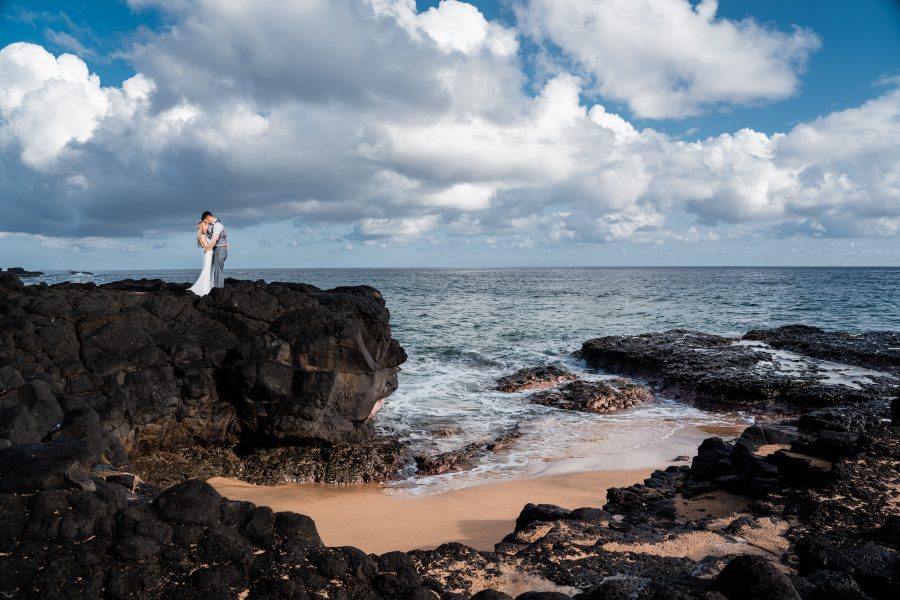 Bride and groom getting married on a black lava cliff over the ocean in Kauai, Hawaii