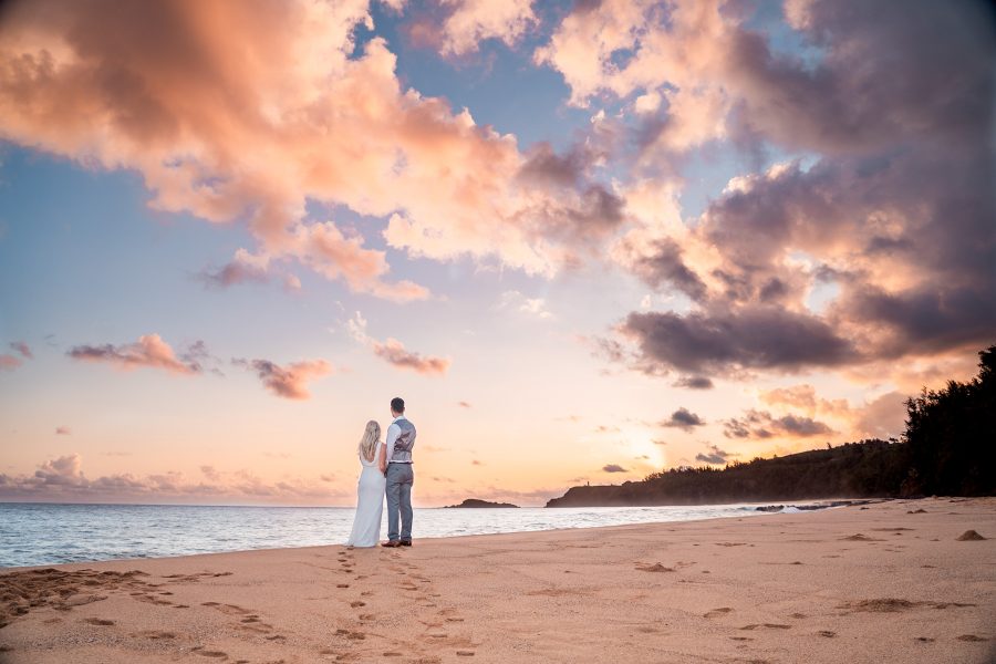 Bride and groom watch the sunrise together on an empty beach in Kauai, Hawaii