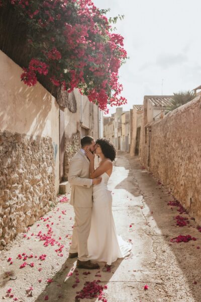 A bride and groom kiss under purple flowers in Mallorca.