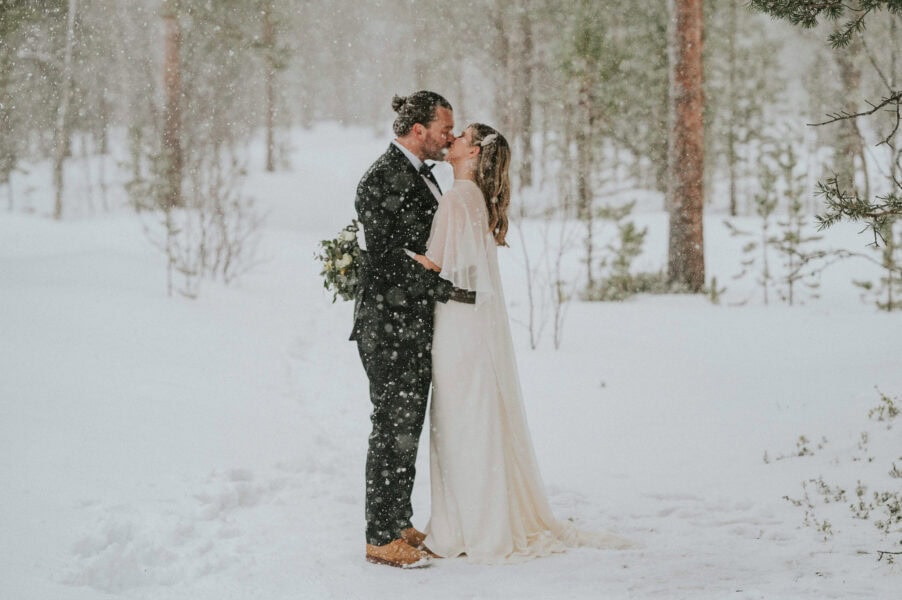 Bridal couple kissing under romantic snowfall on the day of their winter elopement in Norway