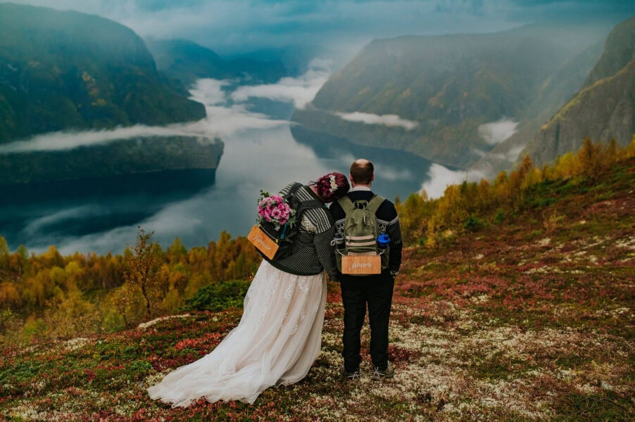 Bride and groom with backpacks hugging each other in front of a gorgeous landscape in Aurland Norway