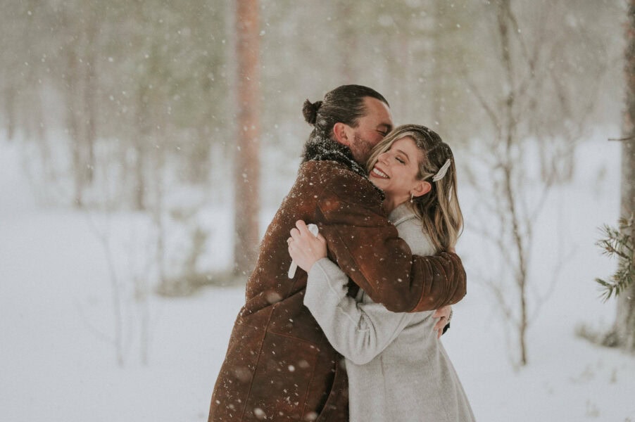 Bridal couple cuddling under romantic snowfall on the day of their winter wedding in Norway