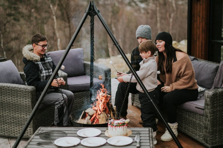 Bride and groom and their kids in cozy winter outfits making s'mores on a campfire outside of the cabin on the day of their elopement in Norway