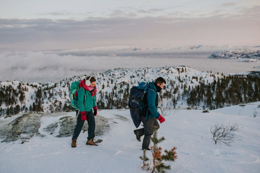 Bridal couple in winter outfits hiking up a snowy mountaintop on the day of their elopement in Alta