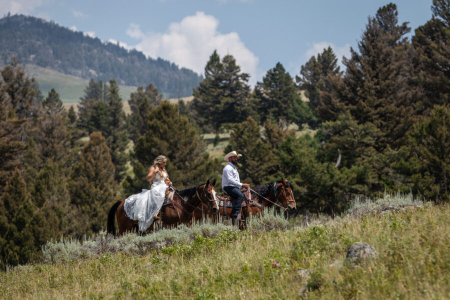 Couple riding horses through a forested mountain meadow