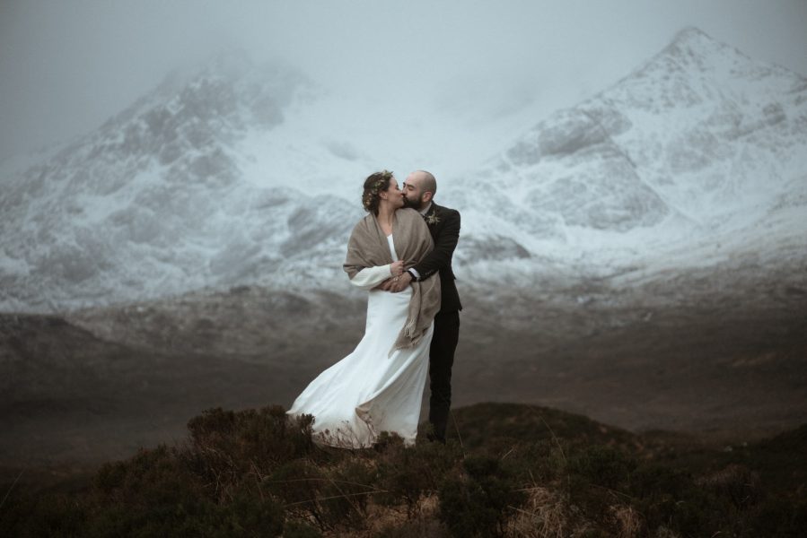 Bride and groom kissing in front of a wintery mountain scene in Scotland