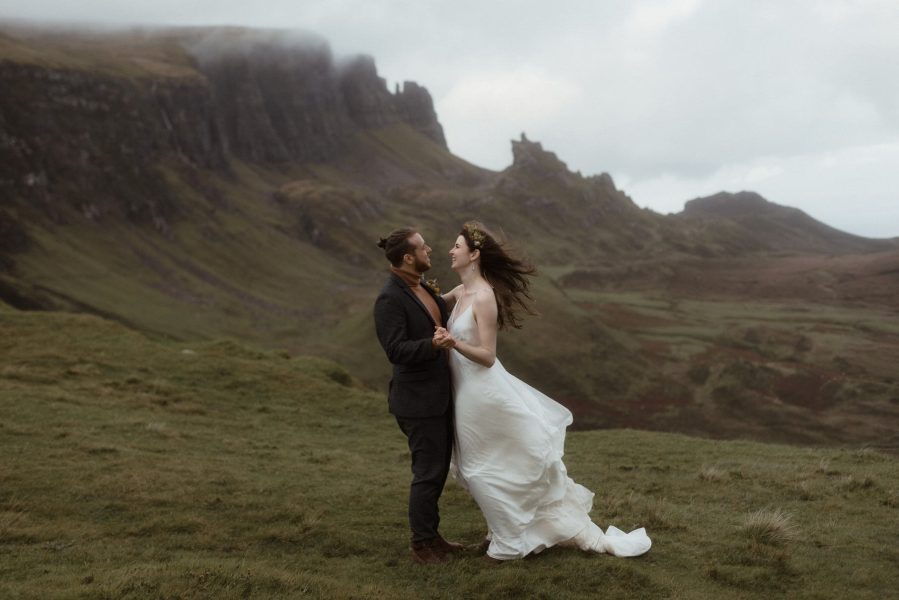 Bride and groom holding hands and dancing on a green mountainside on the Isle of Skye