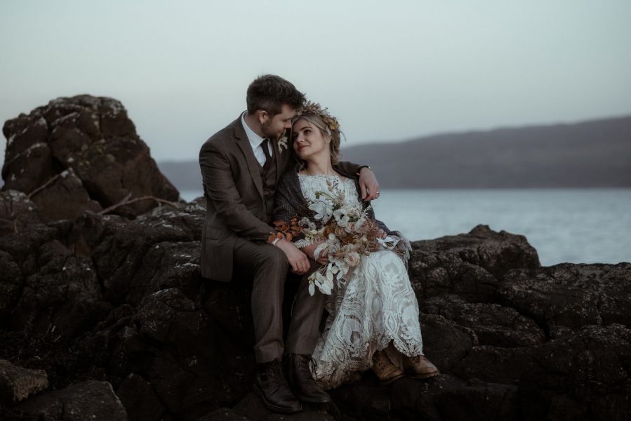 Couple sitting on rocks by the sea at sunset on the Isle of Skye