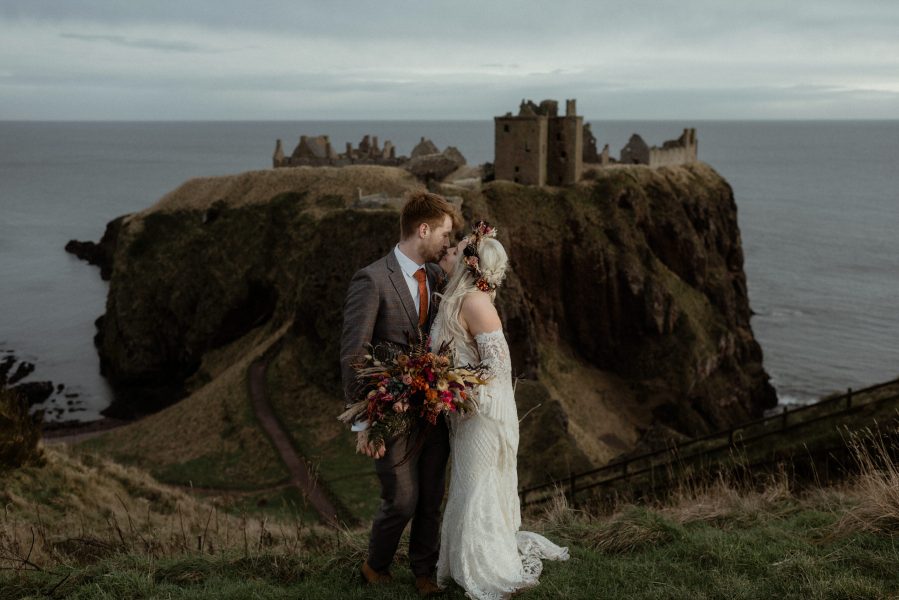 Bride and groom kiss in front of Dunnottar Castle in Scotland