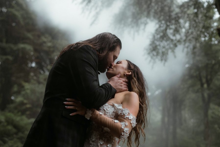 Bride and groom kiss against misty woodland backdrop