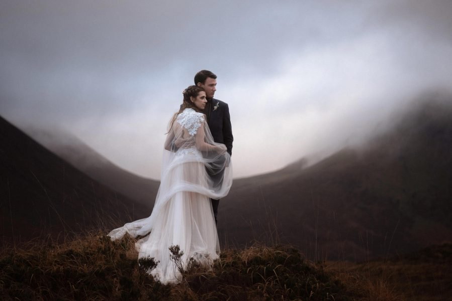 Bride and groom embrace in front of a misty mountain backdrop in the Isle of Skye in Scotland