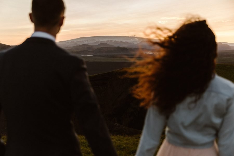 A couple standing holding hands looking out into the mountains at sunset.