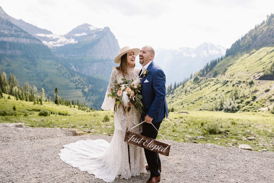 A laughing couple holding a Just Eloped sign in Glacier National Park, MT.
