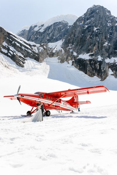Image of a couple eloping by a red plane on a mountain in Alaska.