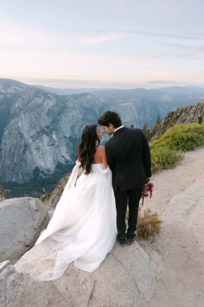 Bride and groom standing on the cliffs of Taft Point in Yosemite at sunset, showcasing breathtaking views of the valley.