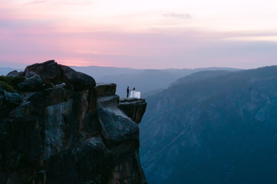 Bride and groom standing hand in hand on the edge of Taft Point in Yosemite, with sweeping views of the valley and dramatic cliffs