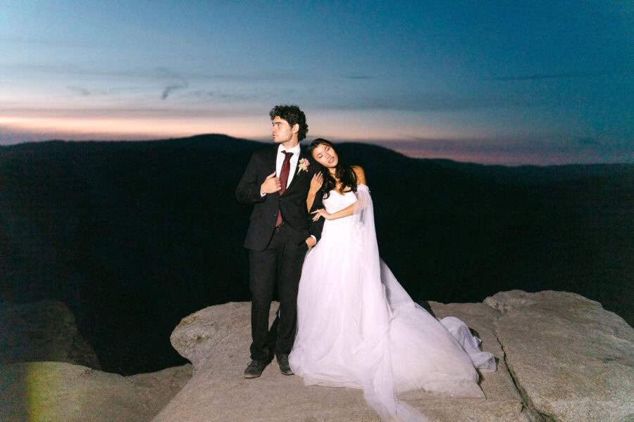 Couple embracing at Taft Point under the night sky, illuminated by a soft flash, with a low glow on the horizon adding a dreamy ambiance.